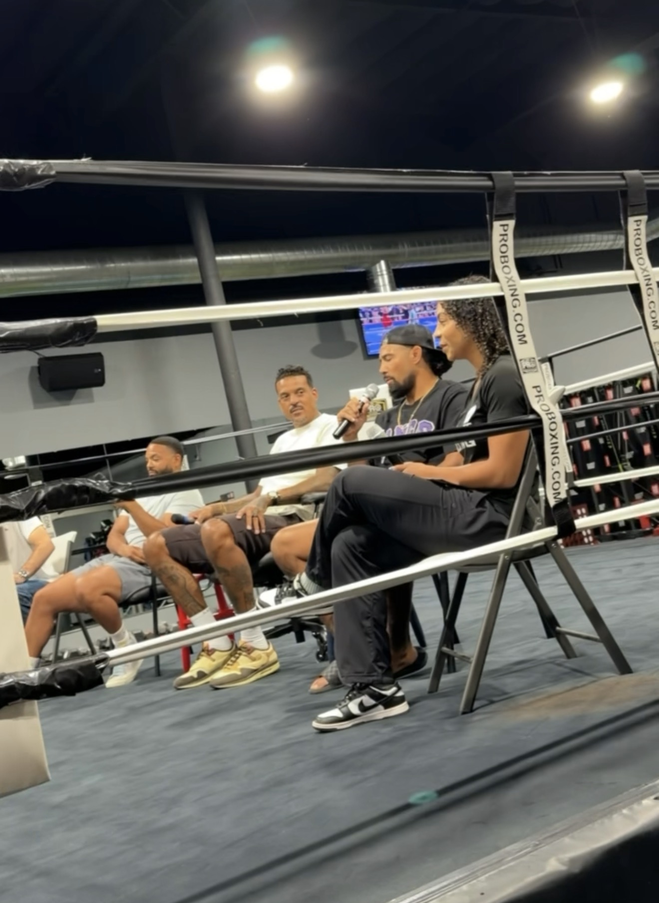 Max speaking into a microphone during a seated panel in a boxing ring
