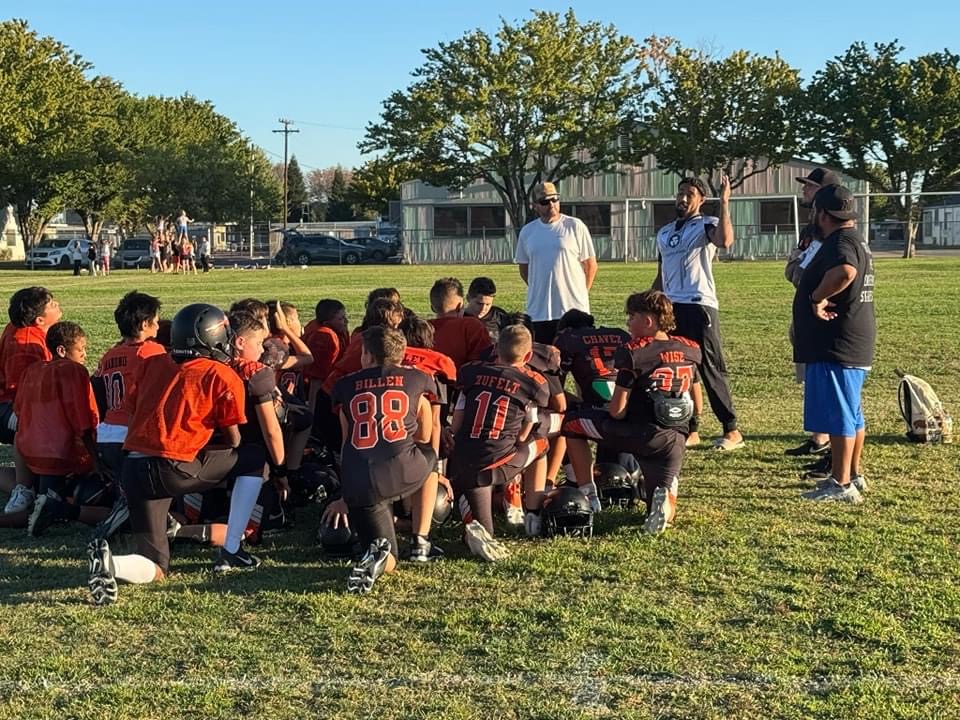 Max speaking to youth football players on a field